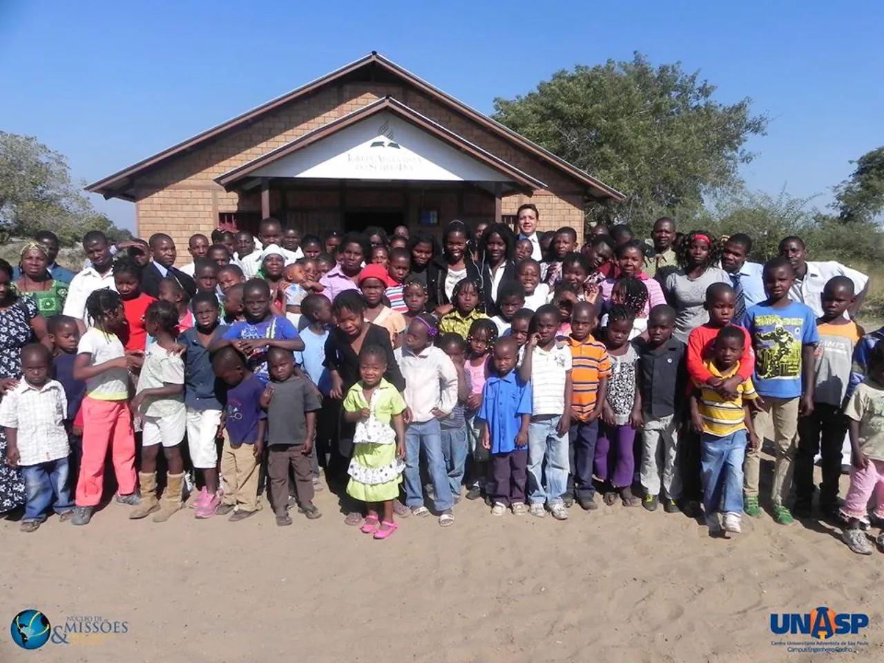 Missionários e crianças reunidos em frente a uma igreja de tijolo ecológico, na África